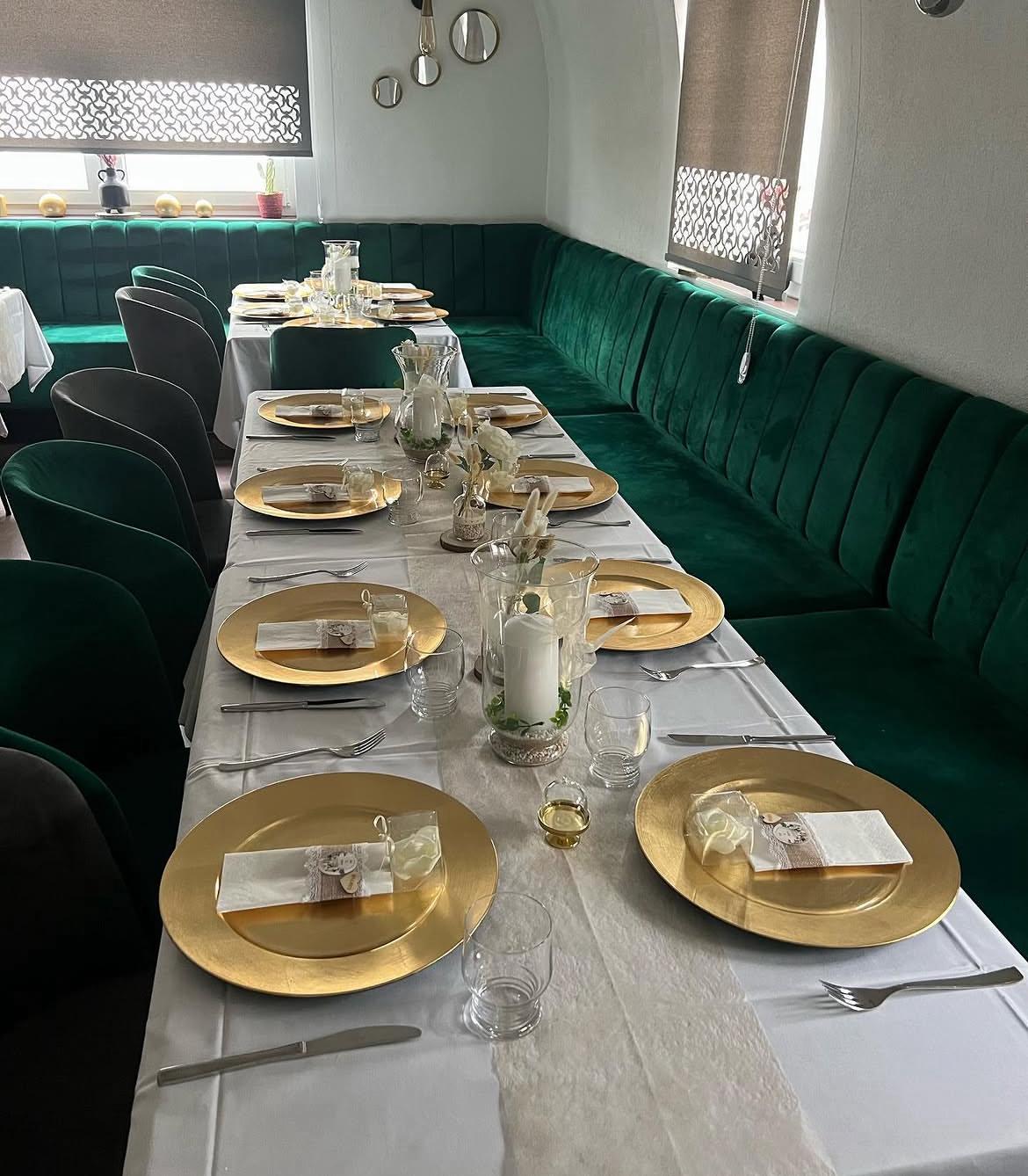 Festlich eingedeckter Saal mit Goldtellern und grünen Bänken